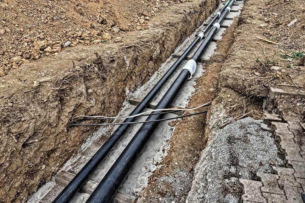 FERNWÄRME Bild zweier Fernwärmeleitungen, die in eine gegrabene Rinne im Boden verlegt werden.