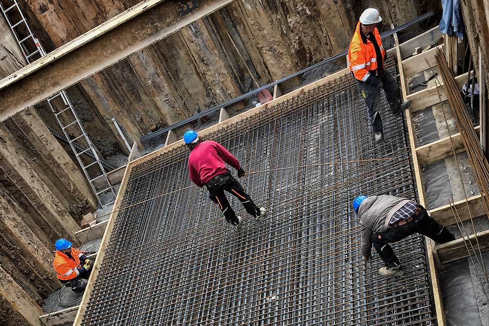 HOCHBAU Ein Bild mit Bauarbeitern, welche Armierungseisen biegen.