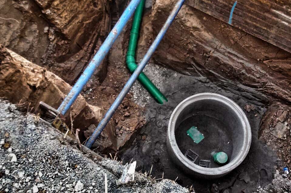 KANALBAU Bild von oben in einen runden Betonschacht blickend mit angeschlossenen Rohrleitungen.